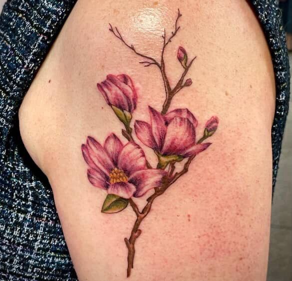 Pink magnolia flower tattoo on skin, with green leaves and a brown branch