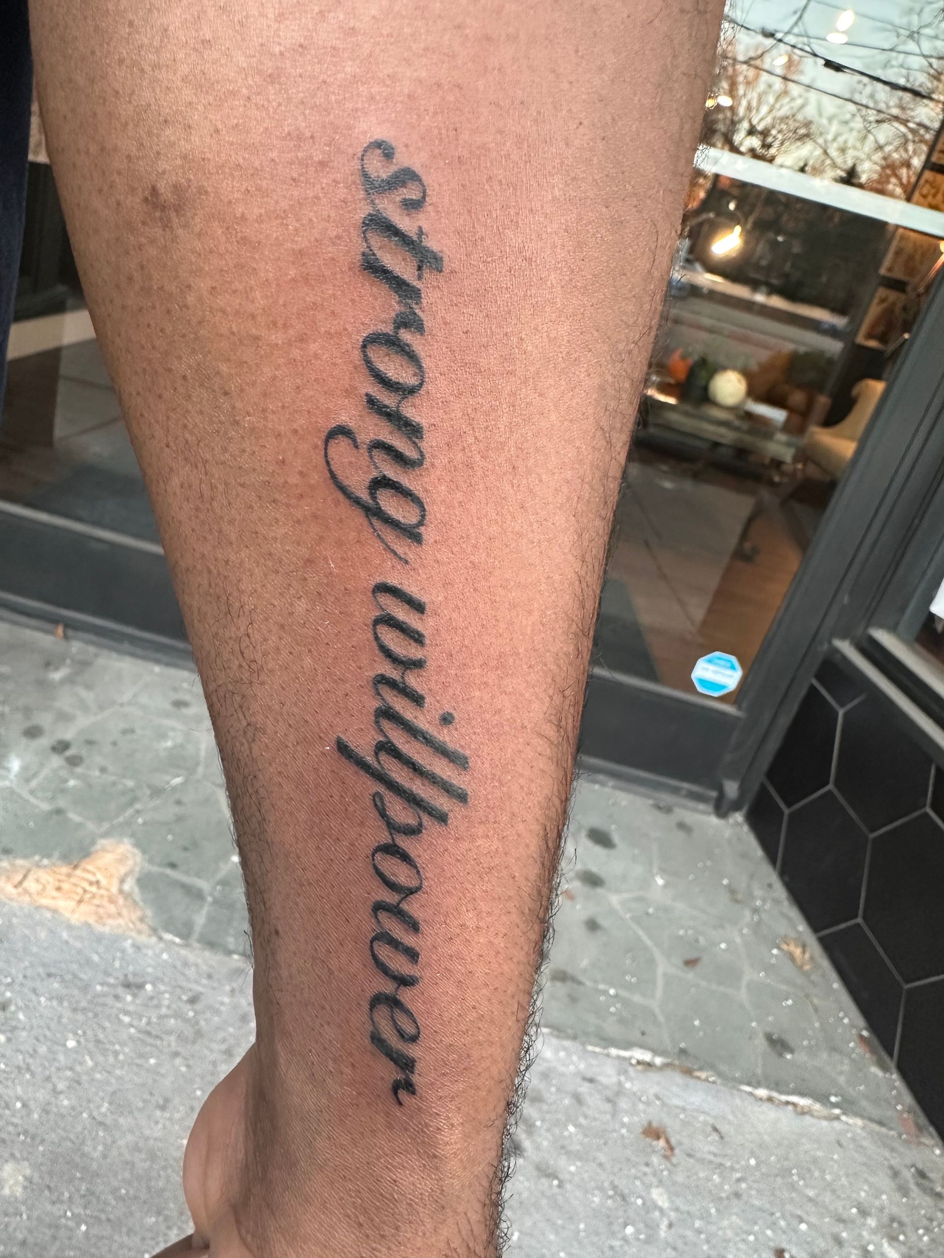 Lower leg tattoo reading “strong enough” on calf, black script on skin.