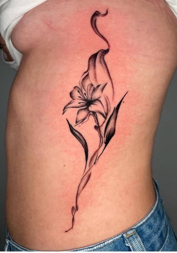 Black floral tattoo on a person's side, with a flower and flowing vine design.