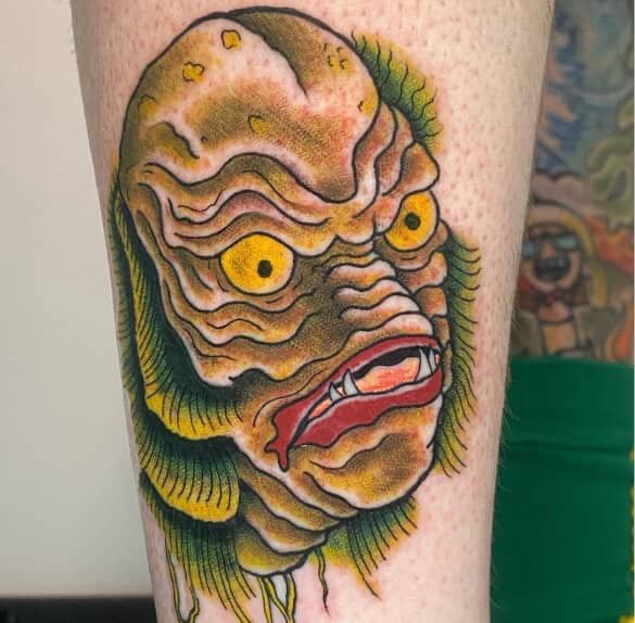 Colorful tattoo of a wrinkled monster face with yellow eyes and red lips on skin