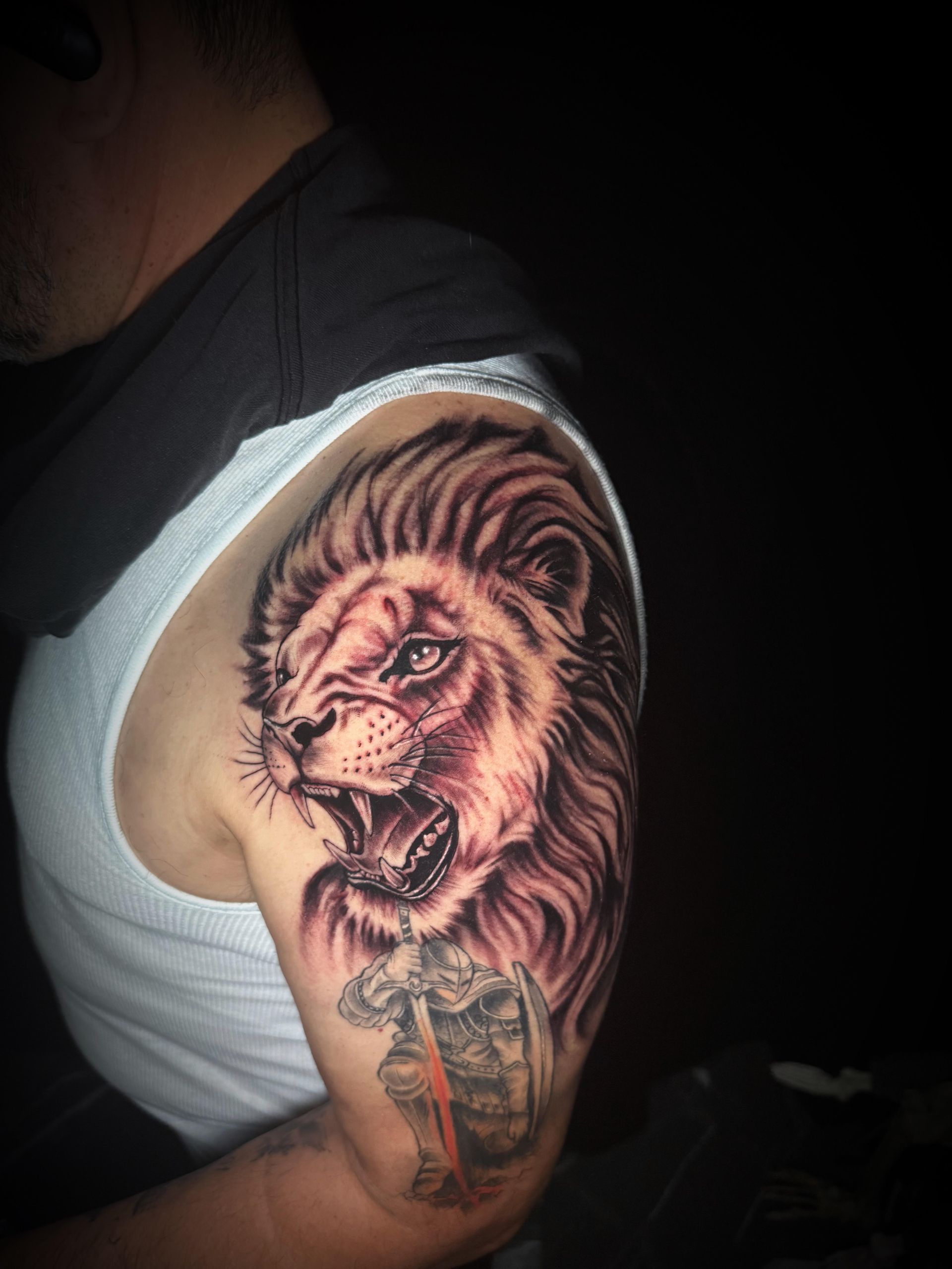 Close-up of a lion tattoo on an upper arm, with a white tank top in the background