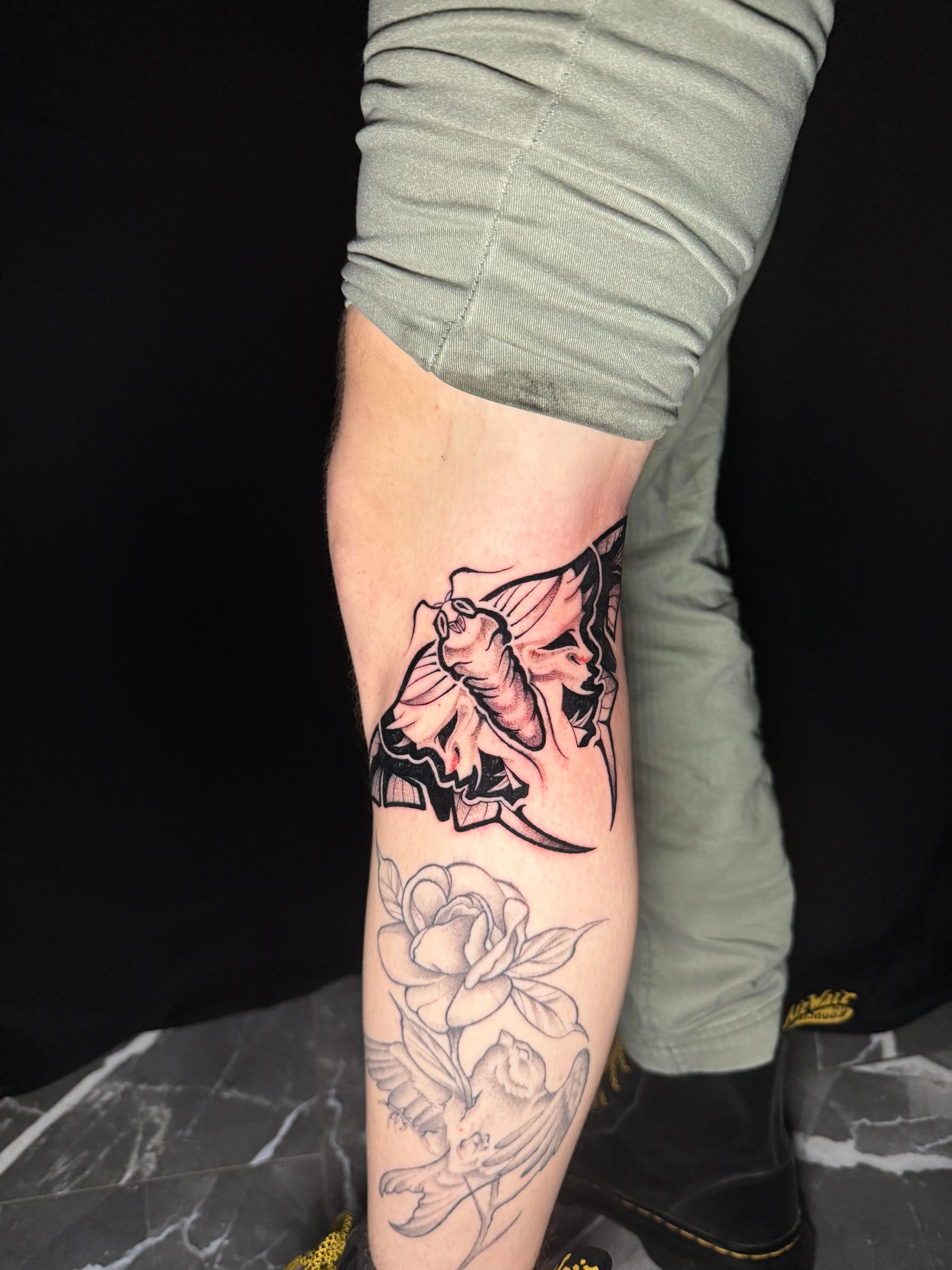 Lower leg with a butterfly tattoo stencil above a floral outline, under rolled gray pants.