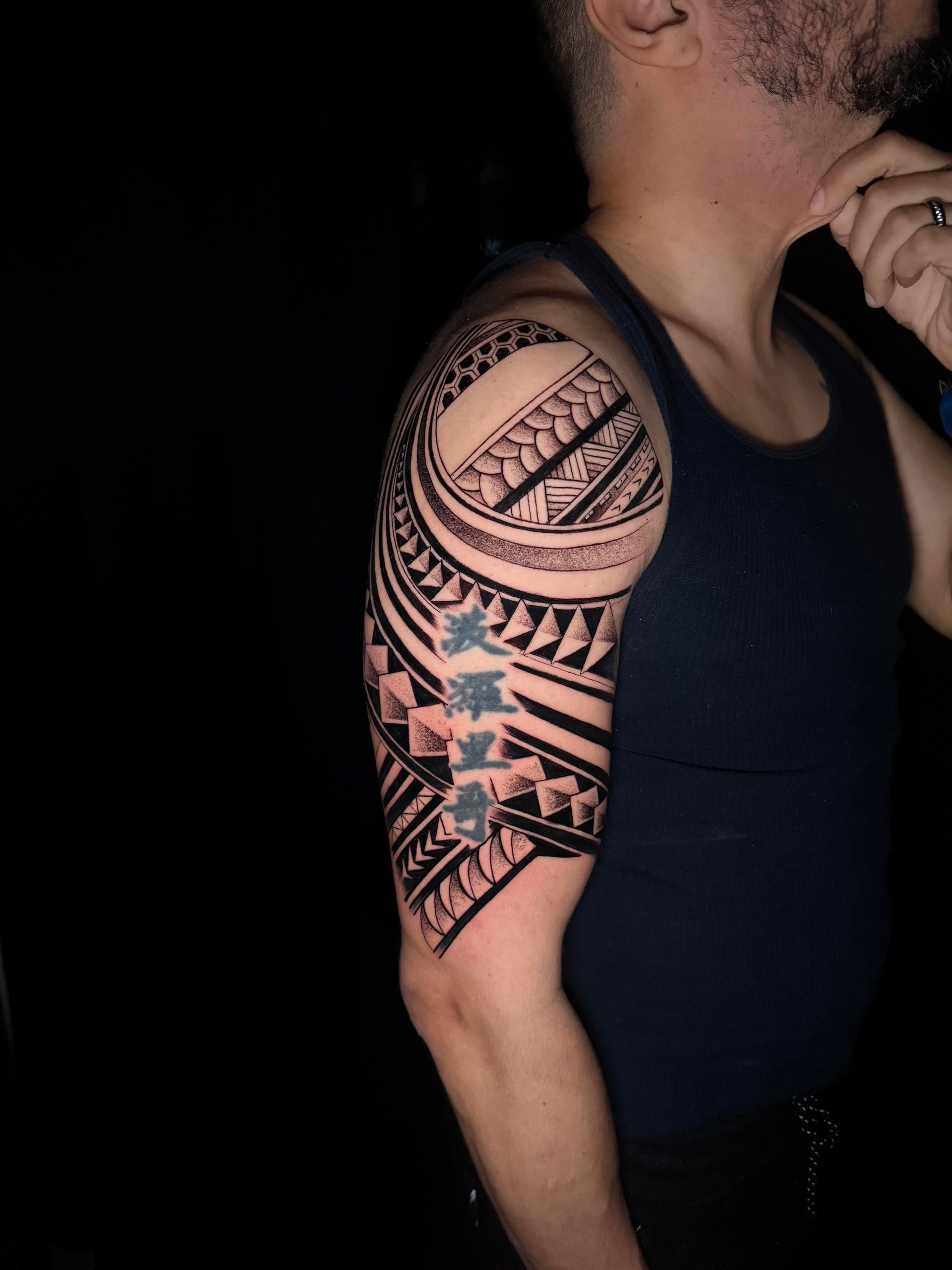 Tattooed upper arm and shoulder of a person in a black tank top against a dark background