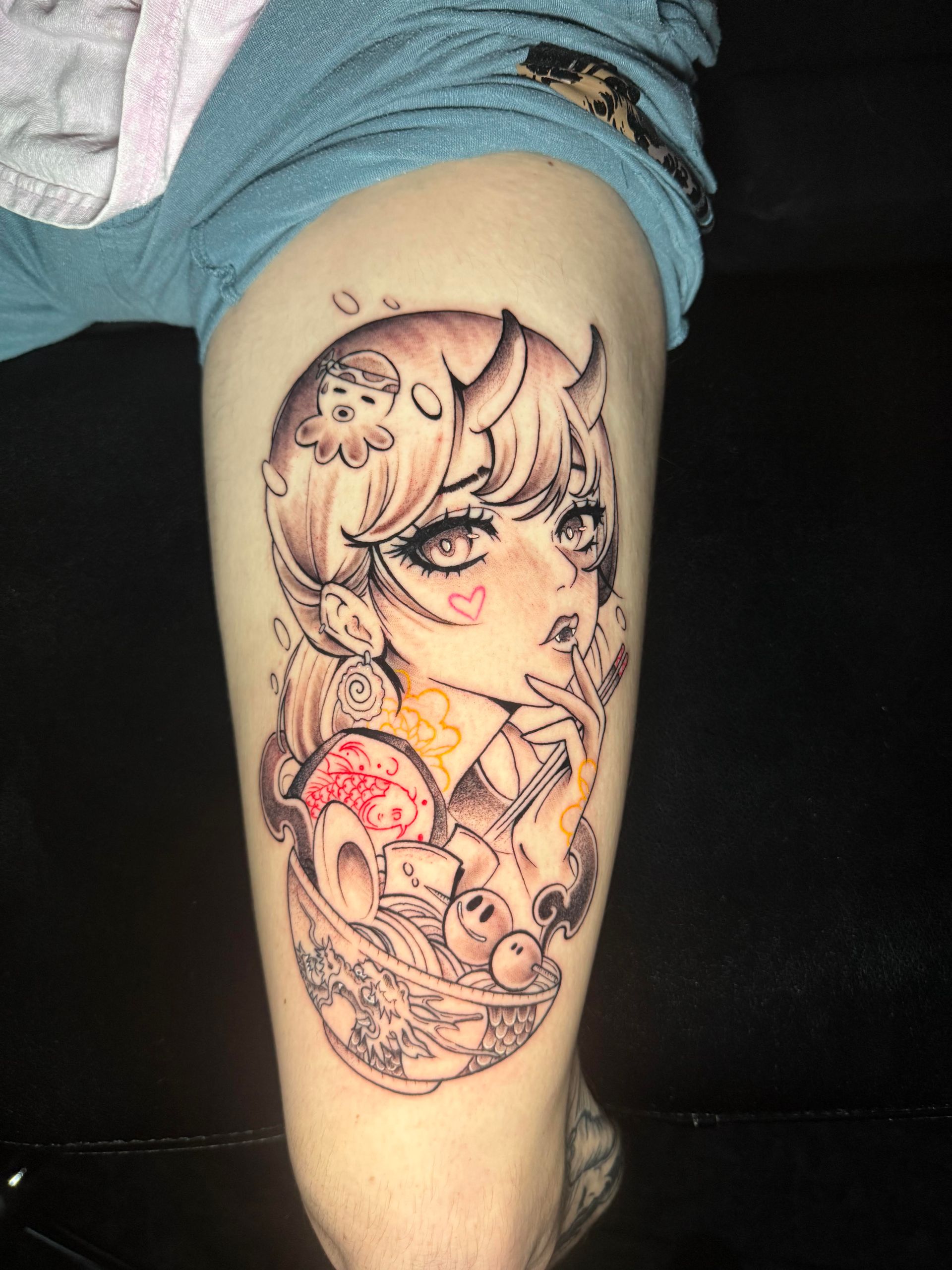 Cartoon-style black-and-red tattoo on a person’s upper arm, featuring a large-eyed character and floral details