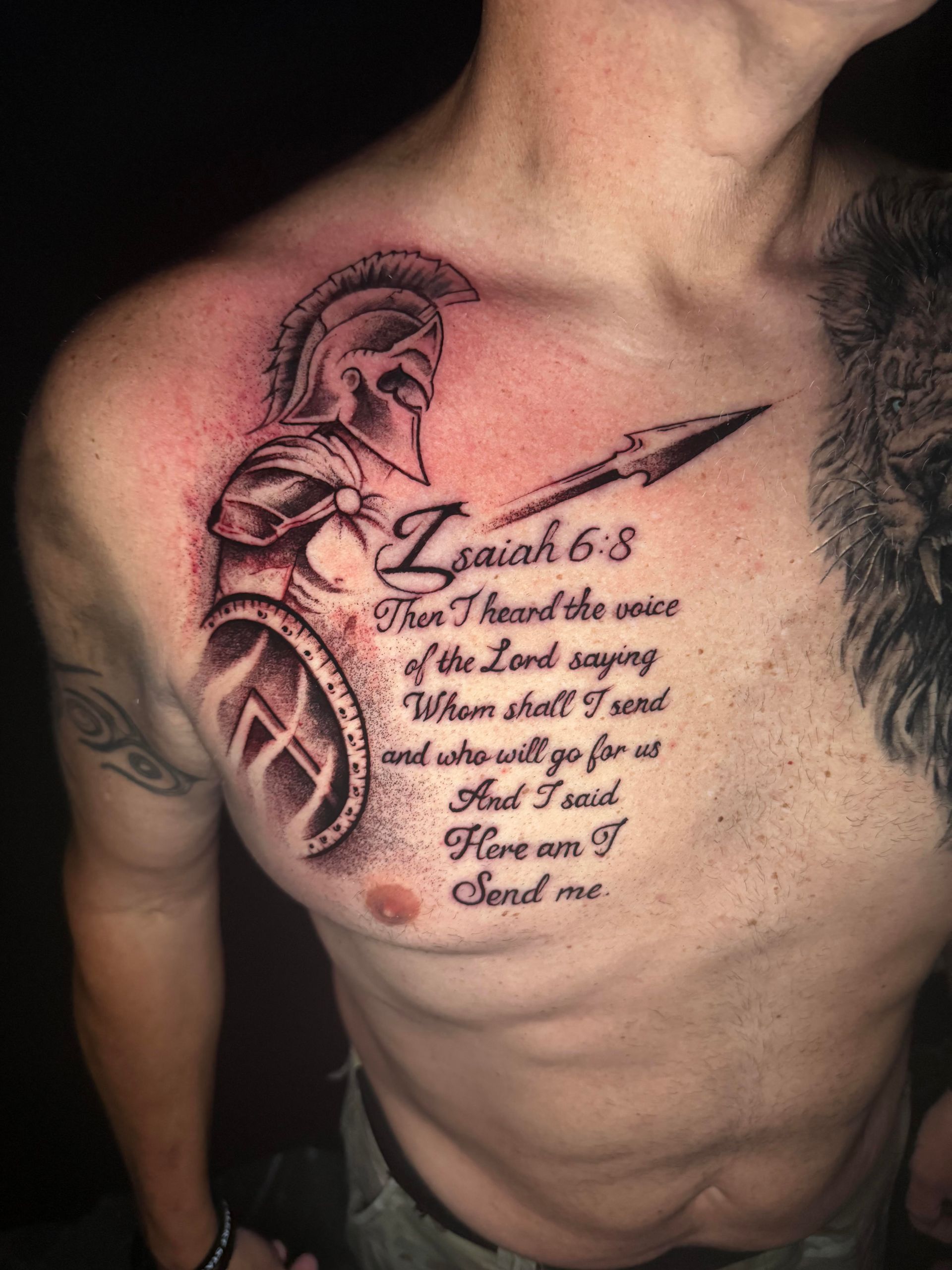 Close-up of a man’s tattooed chest with a Spartan helmet, scripture text, and a cross ornament