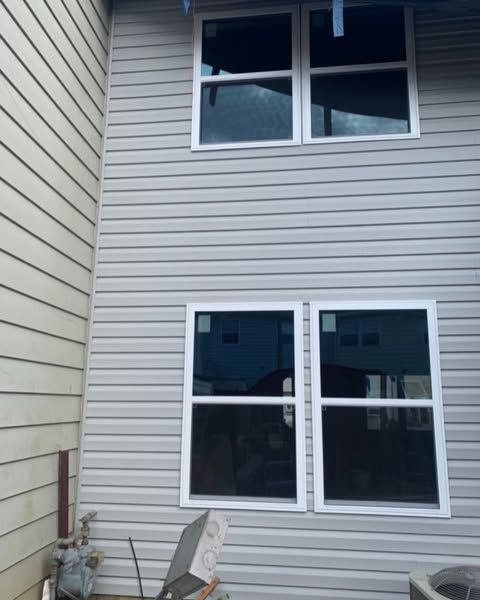 White-sided house exterior with two upper windows and two lower windows beside a narrow gap between buildings
