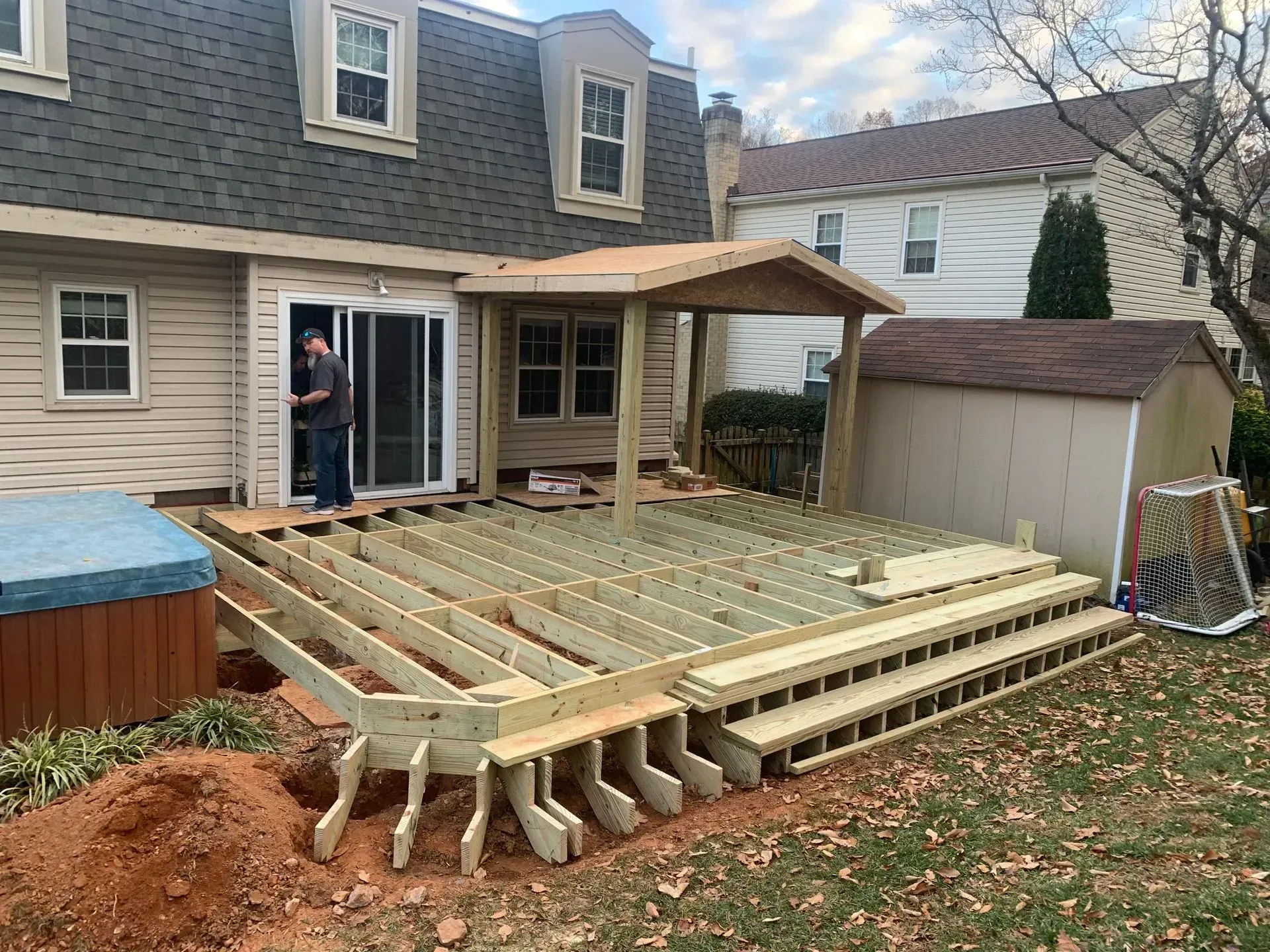 Backyard deck under construction beside a house, with exposed joists and a hot tub nearby