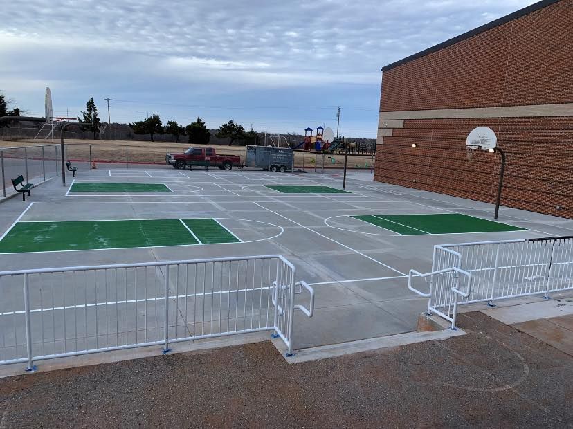 A basketball court with a fence around it and a brick building in the background.