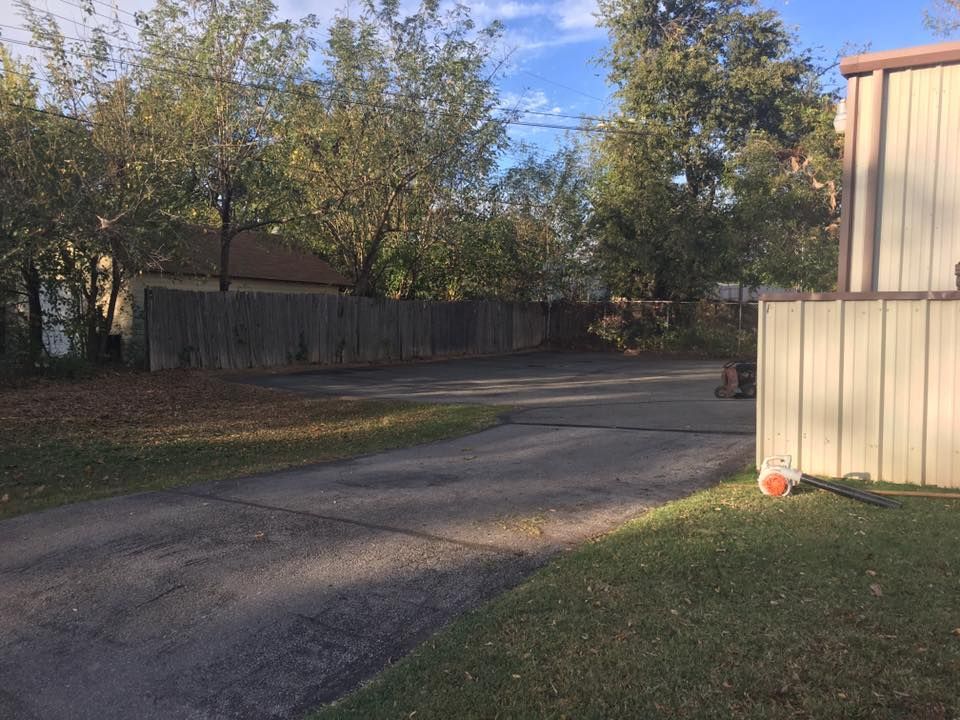 A driveway leading to a house with a fence and trees in the background.
