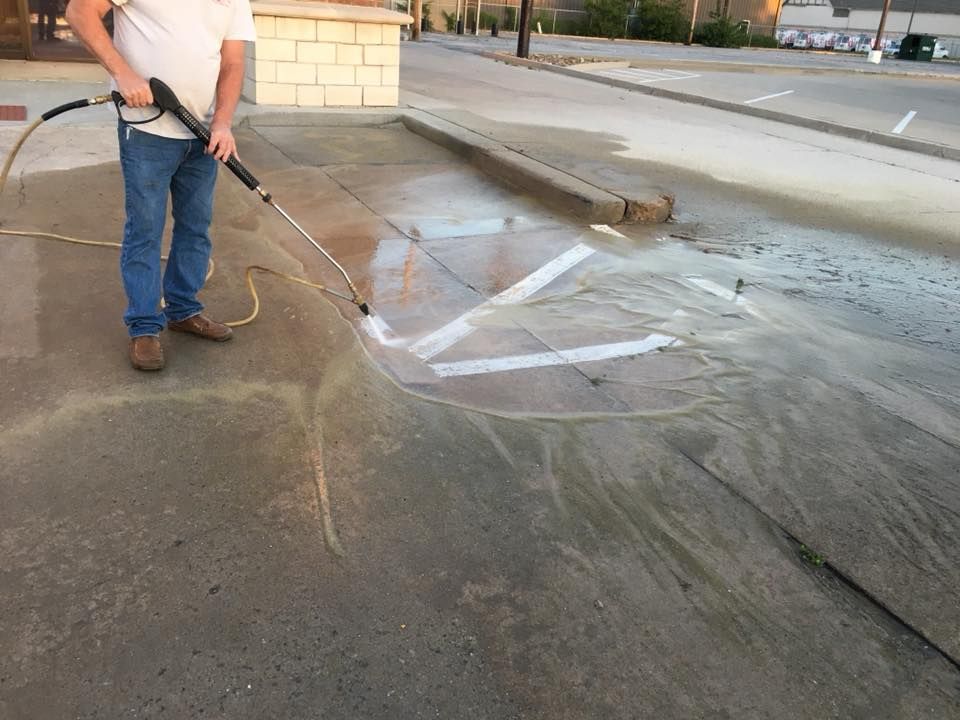 A man is using a high pressure washer to clean a sidewalk