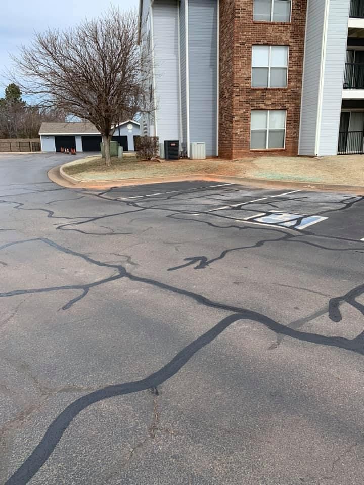 A cracked asphalt road in front of a building with a tree in the background.
