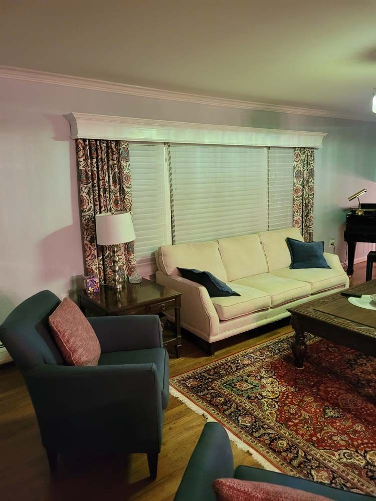 Living room with floral drapes, cream sofa, blue armchairs, and a Persian rug.
