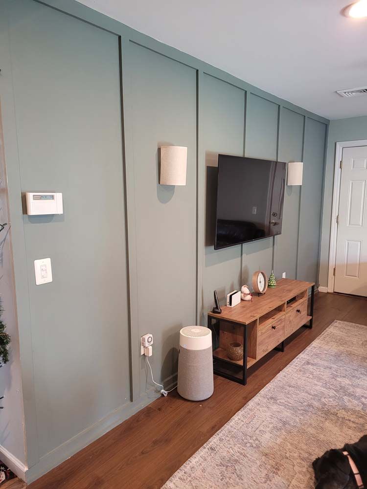 A teal accent wall with a mounted TV, speakers, and wooden media console in a living room.