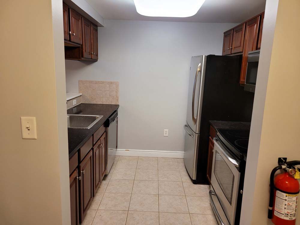 Kitchen with dark wood cabinets, stainless steel appliances, and beige tile floor.