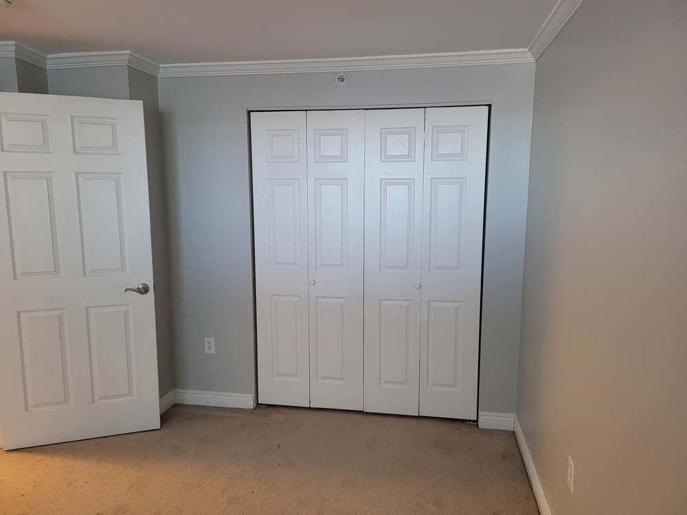 White bi-fold closet doors and a white door on a gray wall in a room with a carpeted floor.