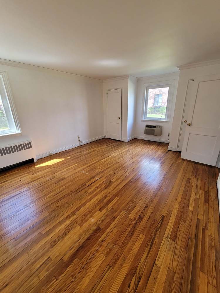 Empty room with hardwood floors, white walls, two doors, and a window.