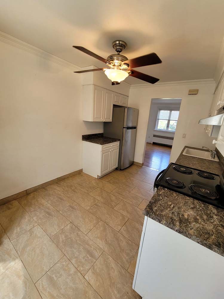 Kitchen with white cabinets, brown countertops, and tile flooring; view of a stove and a doorway.
