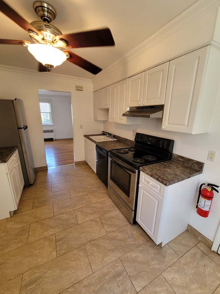 White kitchen with stainless steel appliances, brown countertops, and tile flooring. A red fire extinguisher is mounted.