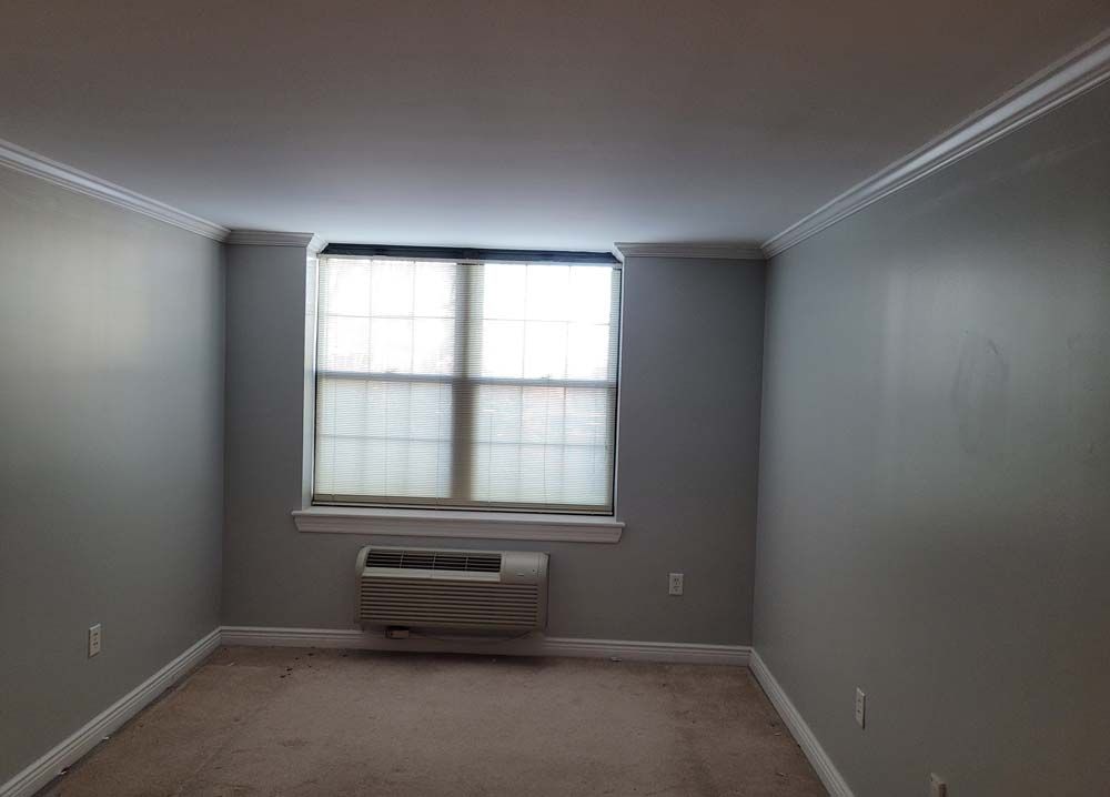 Empty room with gray walls, window with blinds, and air conditioning unit.