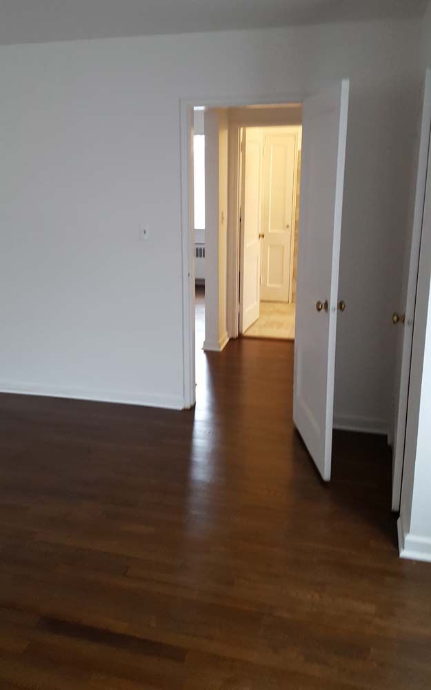 Empty room with dark wood floor, white walls and trim, and open doorways.