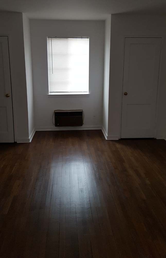 Empty room with dark wood floor, window, and two white doors.