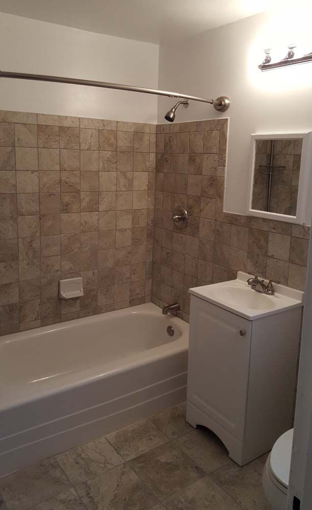 Bathroom with white tub, vanity, and tan tile walls. A mirror and shower fixtures are visible.