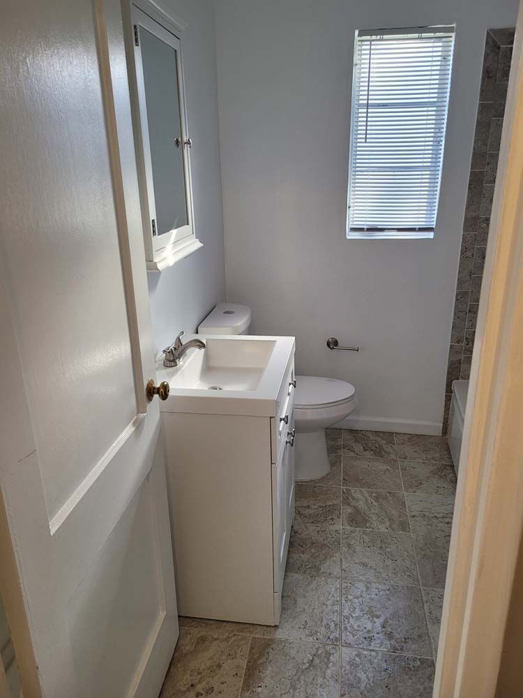 Bathroom with white vanity, toilet, and window with blinds; gray tile floor.