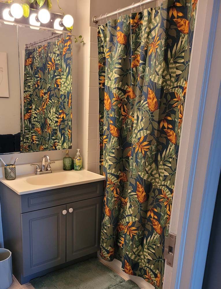 Bathroom with blue vanity, floral shower curtain, and mirror reflecting the scene.