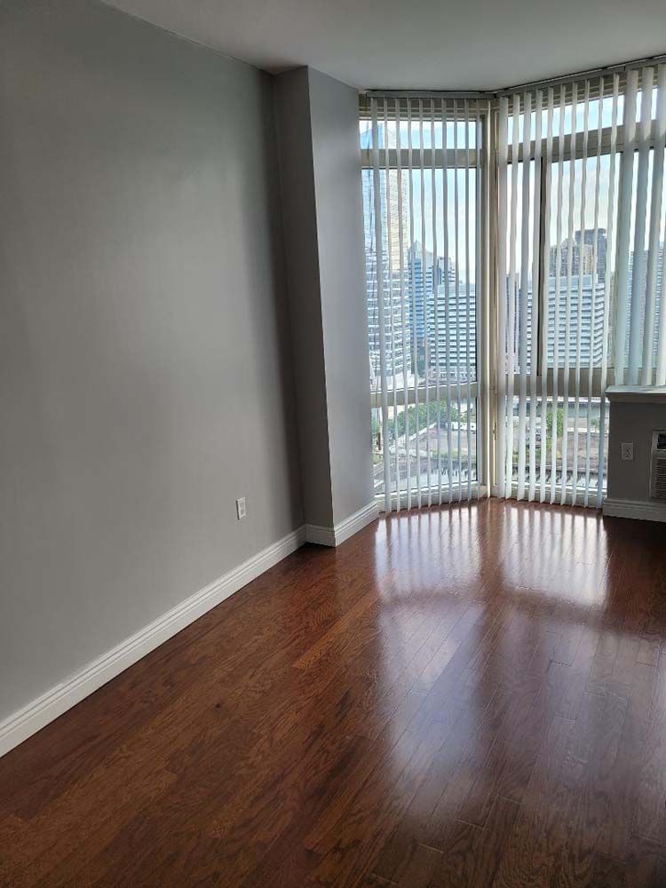 Empty room with hardwood floors, gray walls, vertical blinds, and a city view.