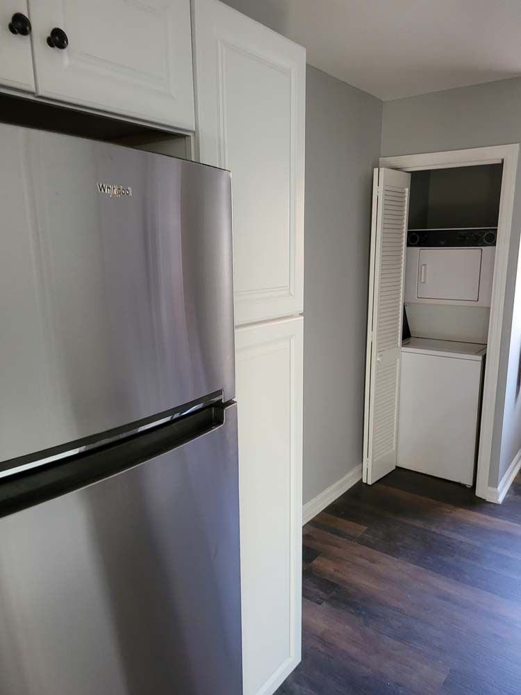 Kitchen with stainless steel refrigerator, white cabinets, and a stacked washer and dryer behind folding doors.