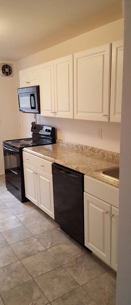 Kitchen with white cabinets, black appliances, speckled countertops, and tile flooring.