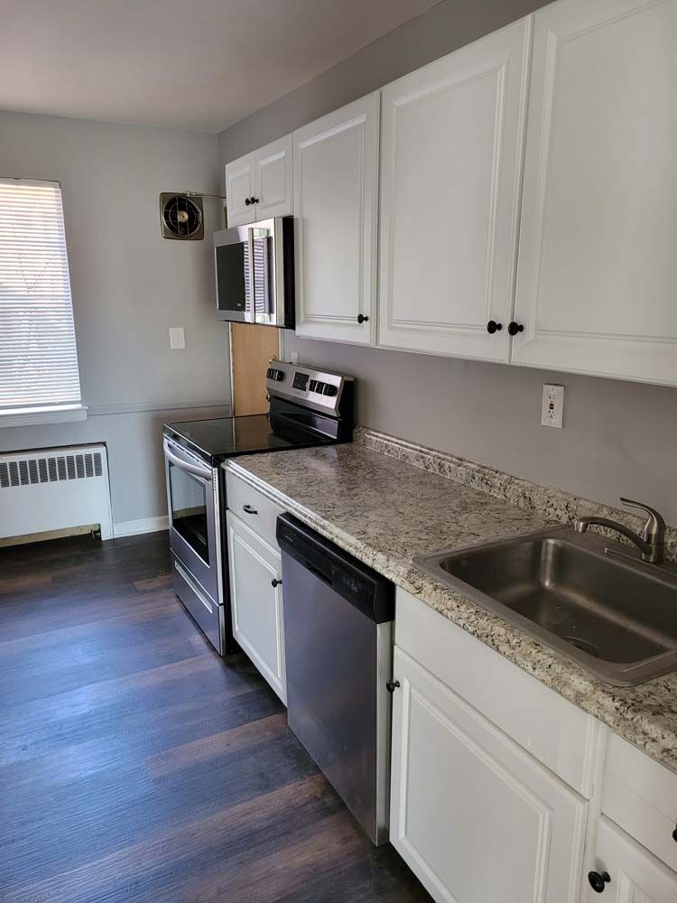 Kitchen with white cabinets, stainless steel appliances, and dark wood-look floor.