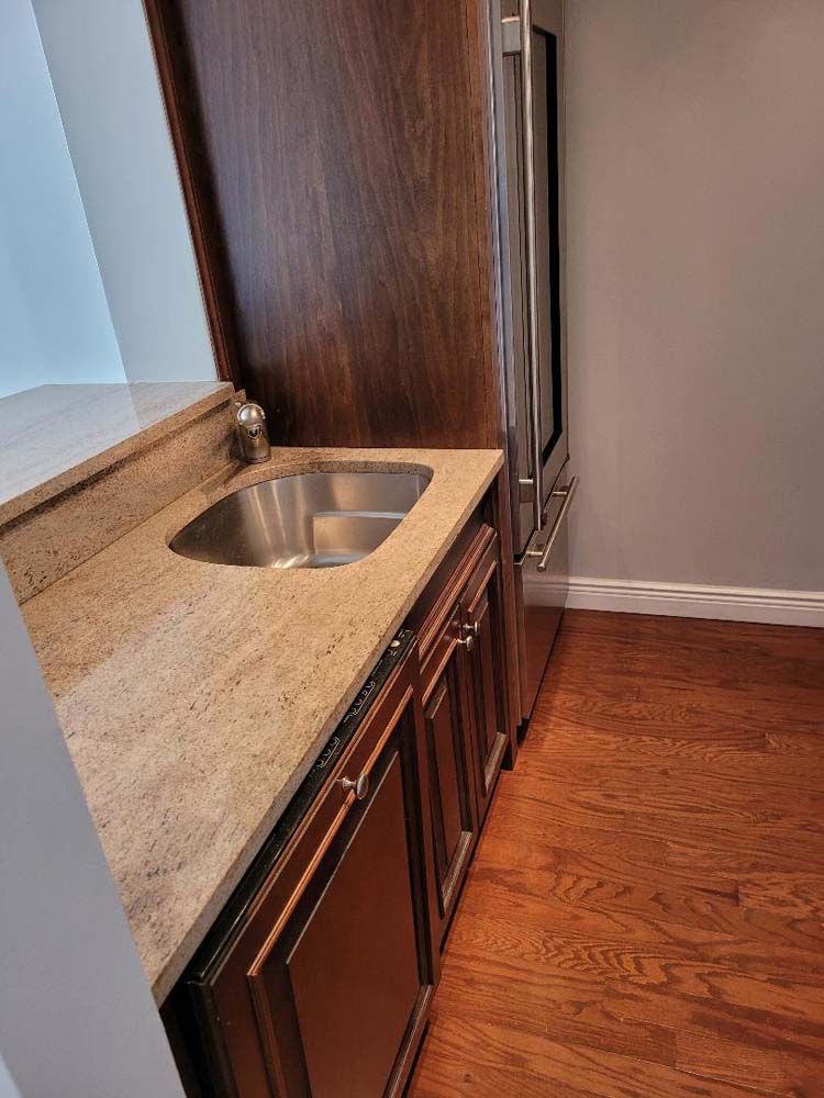 Kitchenette with brown cabinets, granite countertop, stainless steel sink, and wine fridge.