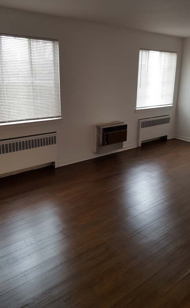 Empty room with dark wood floors, white walls, two windows, and radiators.