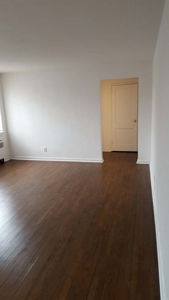 Empty room with dark wood floors, white walls, and a doorway.