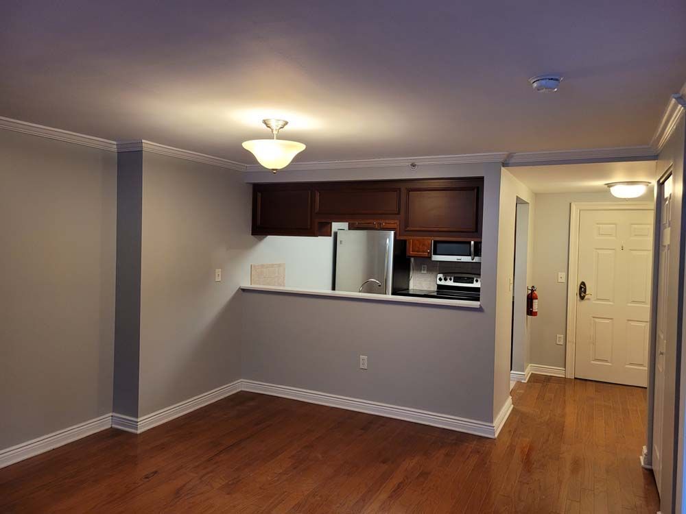Empty apartment interior with kitchen bar, dark cabinets, and hardwood floors.