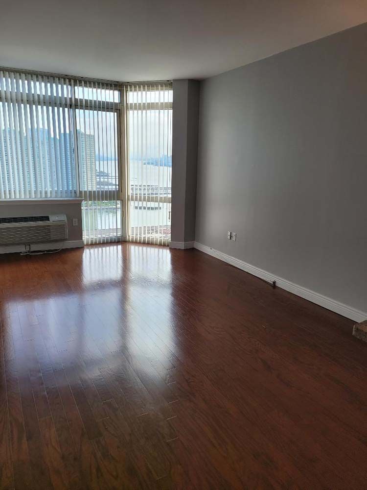Empty living room with wood floors, large windows, and grey walls.