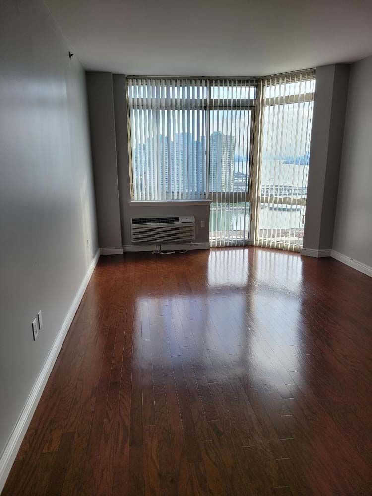 Empty room with hardwood floor and large window with blinds.