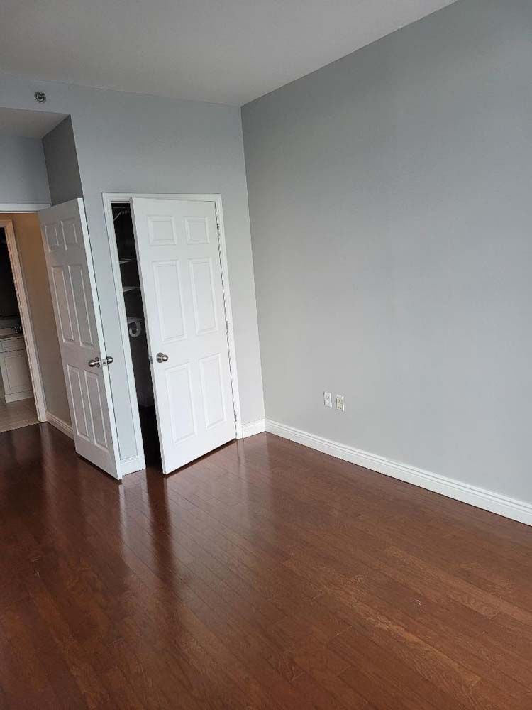 Empty room with hardwood floors, gray walls, white doors, and a closet.