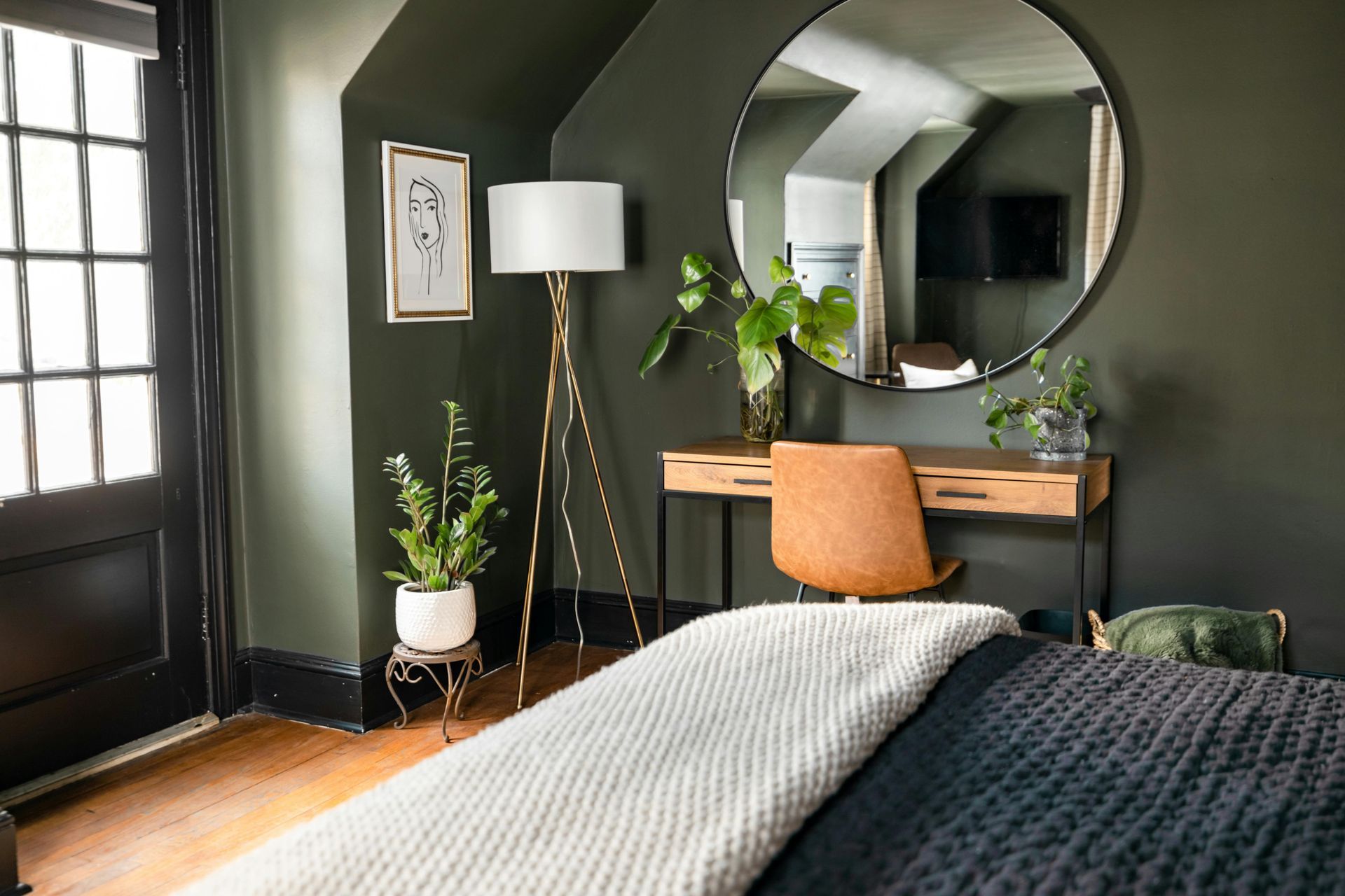 A bedroom with a bed , desk , lamp and mirror.