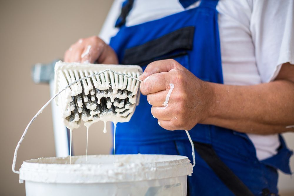 A man is holding a paint roller and a bucket of paint.