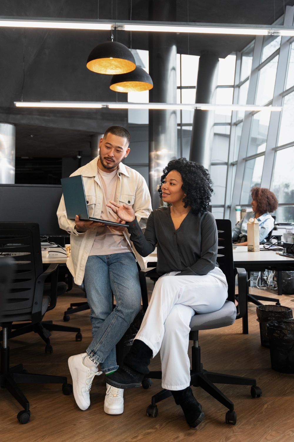 Two professionals collaborating in a modern office space, discussing work on a laptop. A dynamic and creative environment, representing the team culture at VelvetList Media.