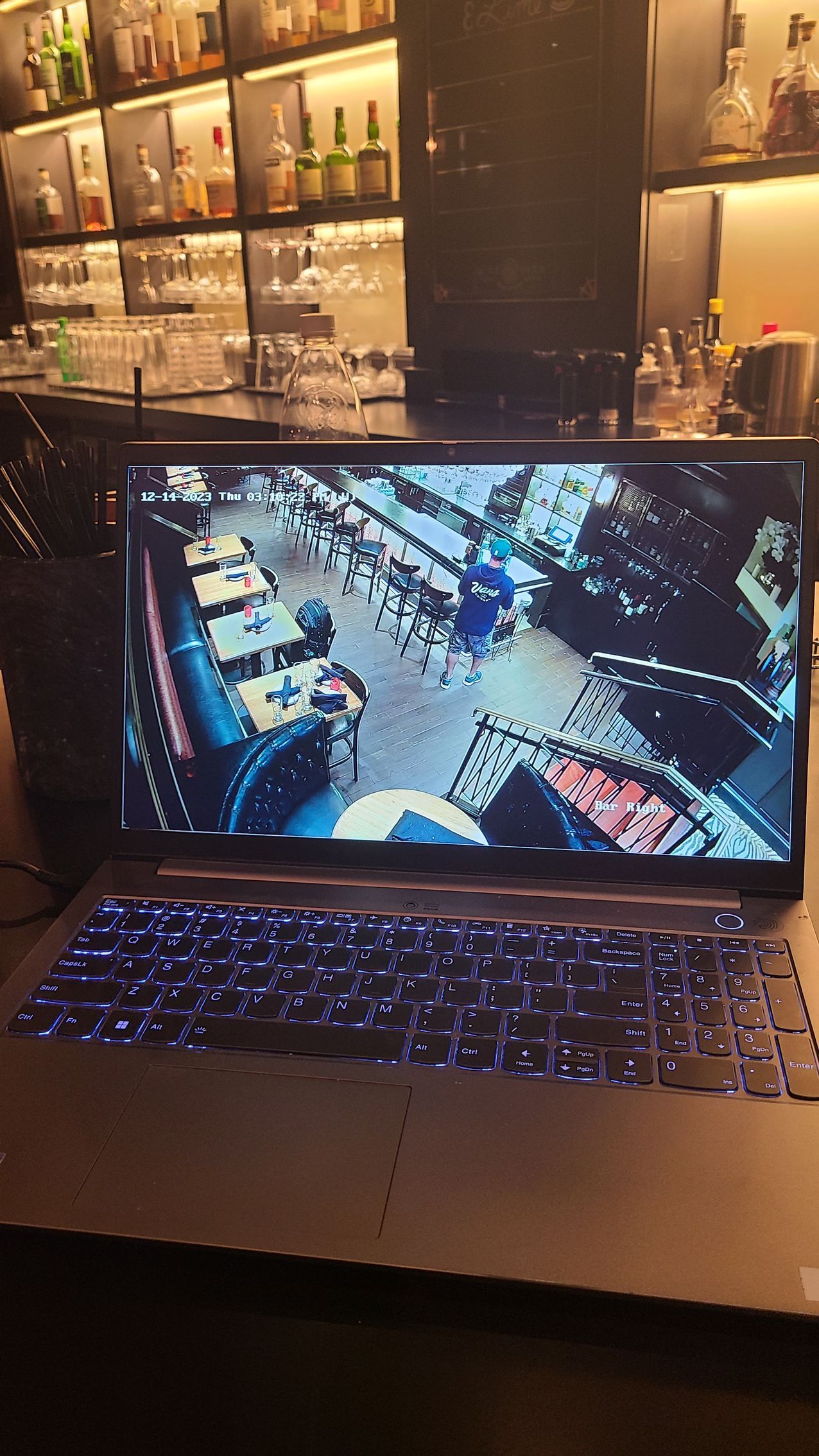 Laptop displaying an aerial view of a city street, lit blue keyboard, set in a bar.