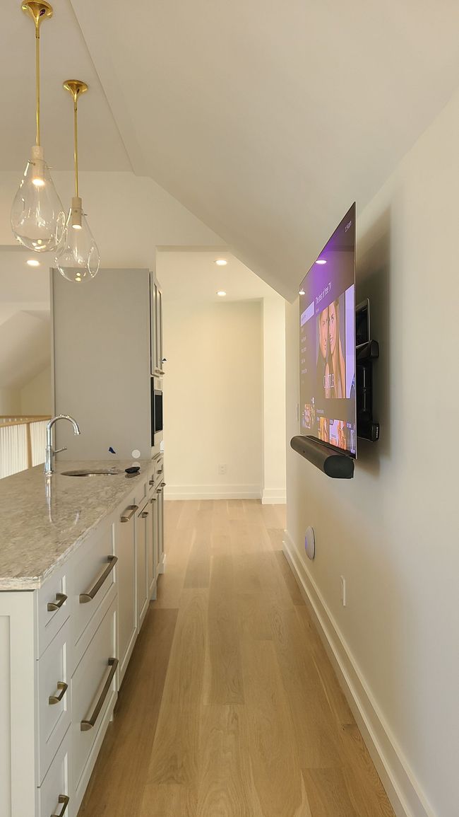 Large TV displays a mountain scene above a black soundbar, with a white marble fireplace below, wooden paneling surrounding.