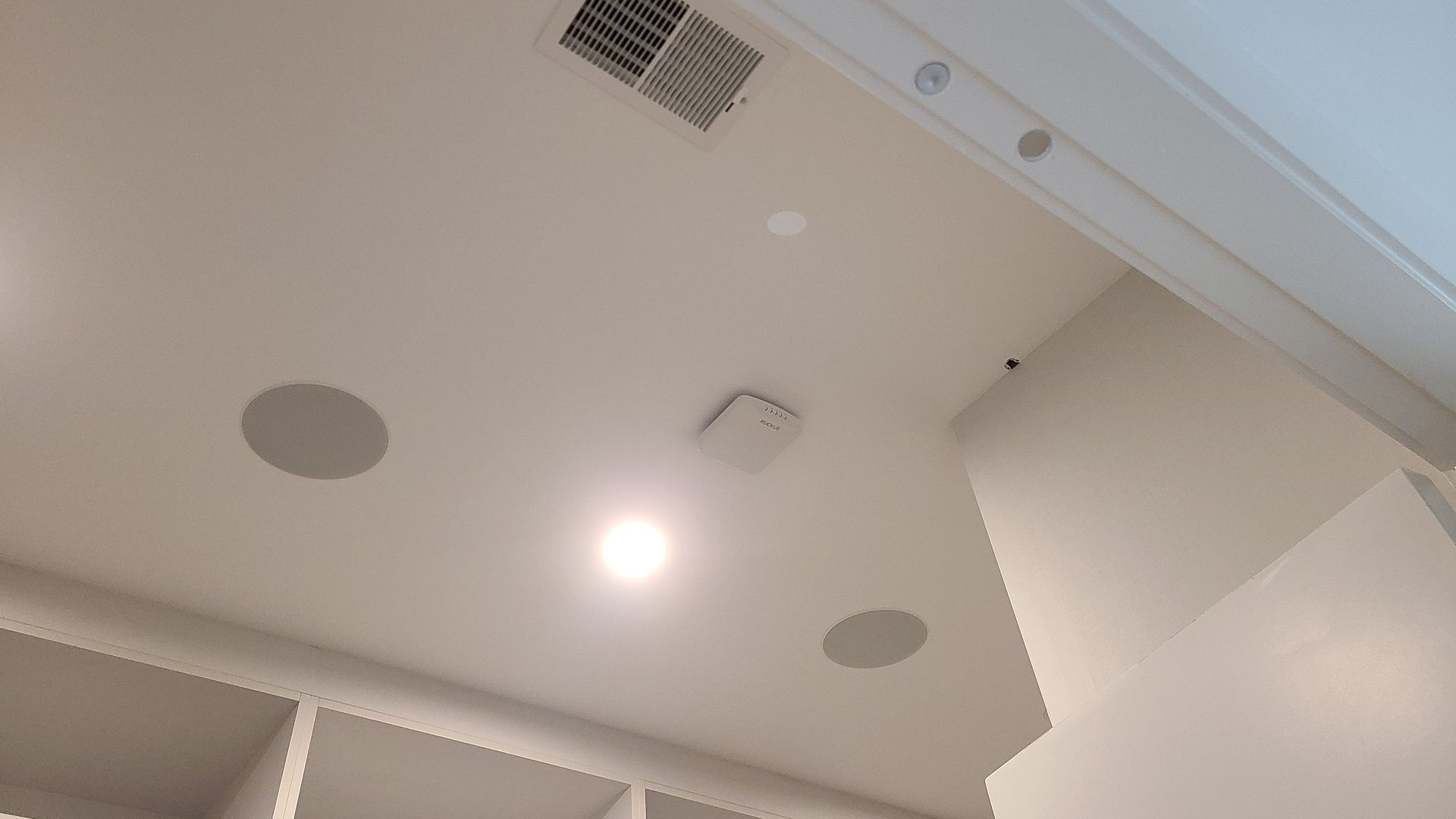 White ceiling with recessed lights, speaker, vent, and a white wall.