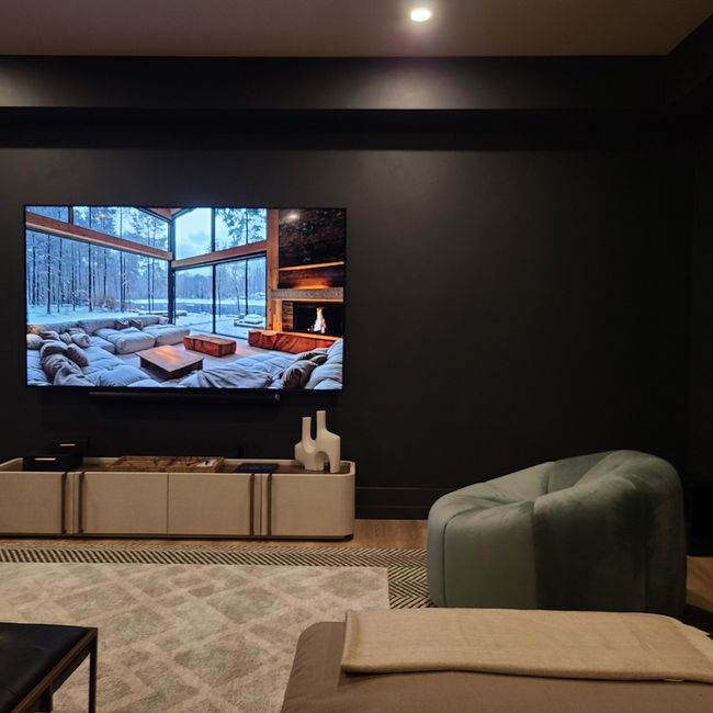Living room with a large TV, off-white cabinet, green chair, and dark gray walls.