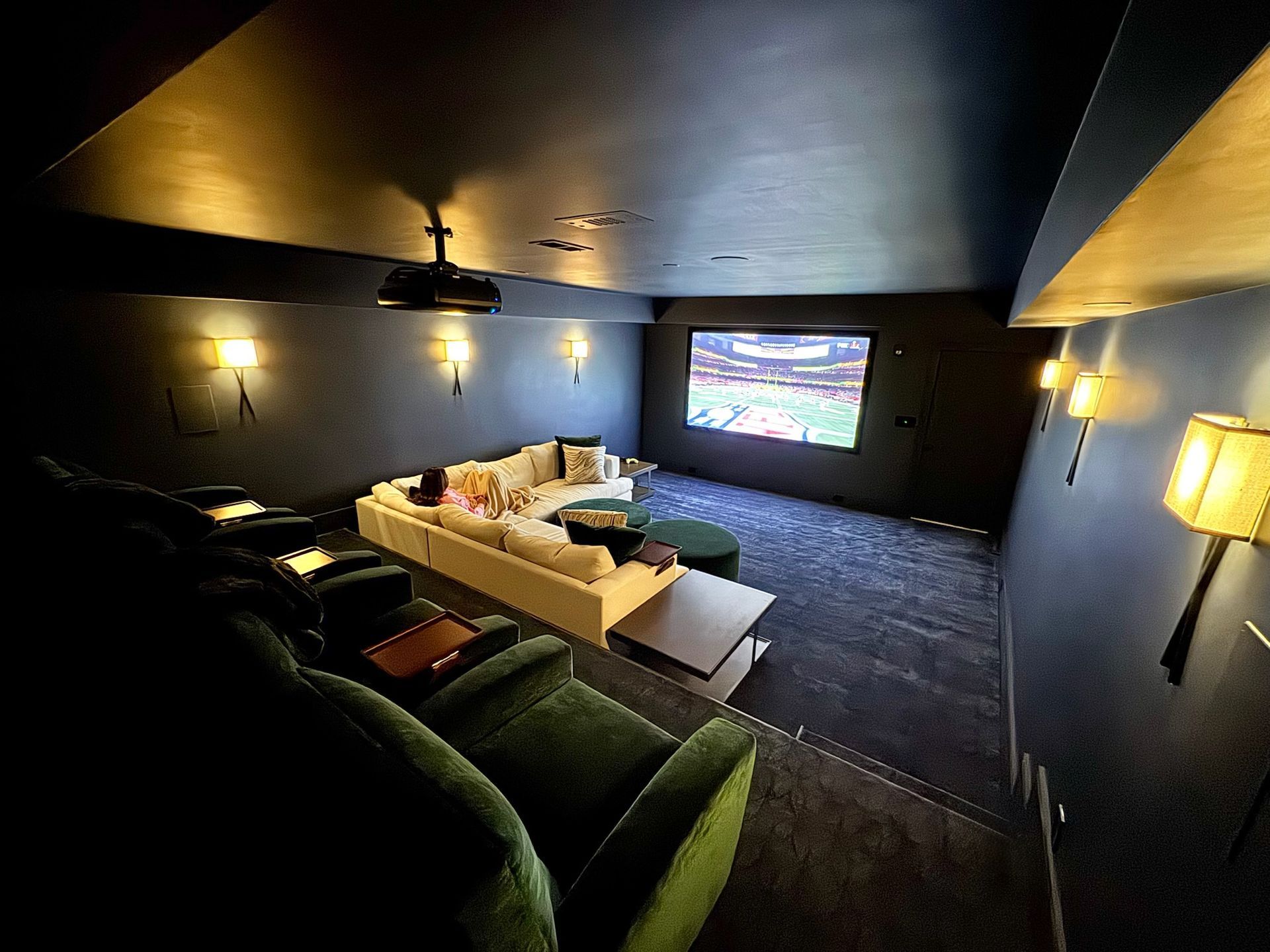 Home theater with white sofas, black walls, large screen, projector, and carpet flooring.