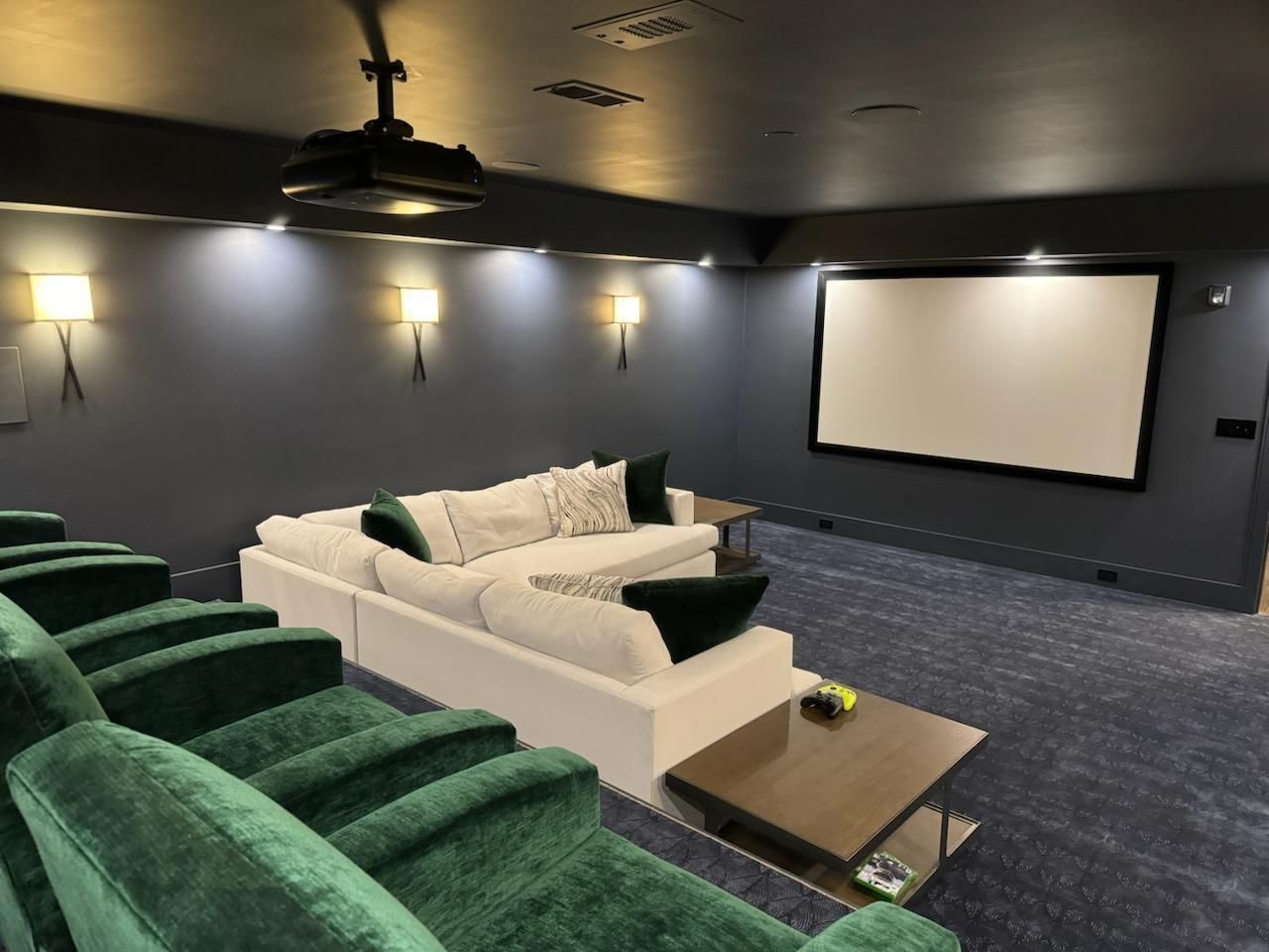 Home theater with green velvet chairs, a white sofa, and a screen on a dark blue wall.