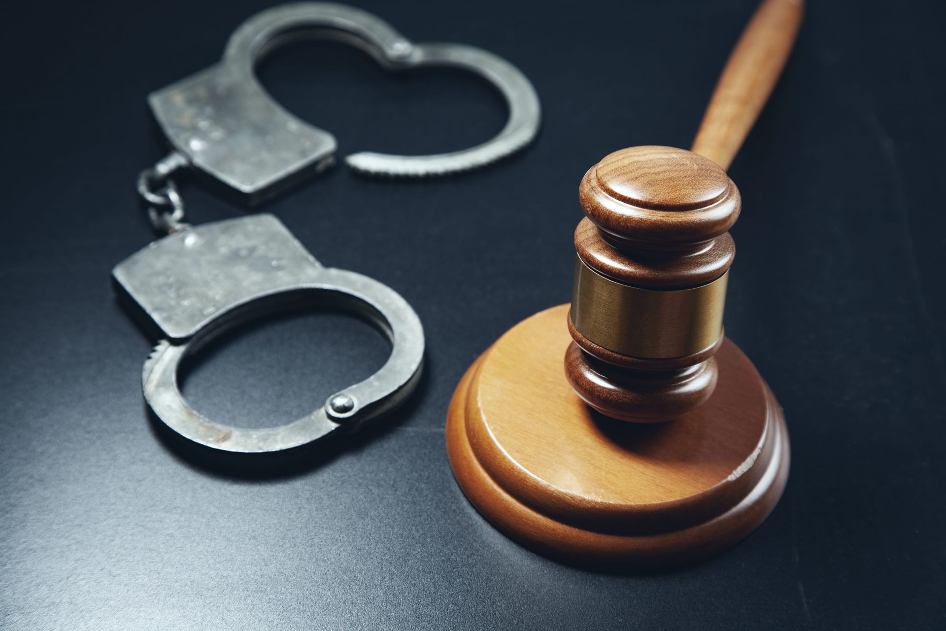 Handcuffs beside a wooden judge’s gavel on a dark background