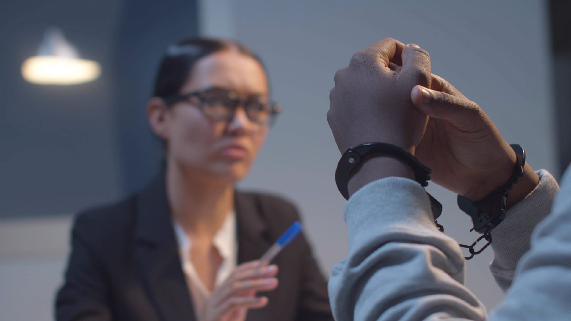 Handcuffed person in foreground facing a blurred professional holding a pen in a meeting room